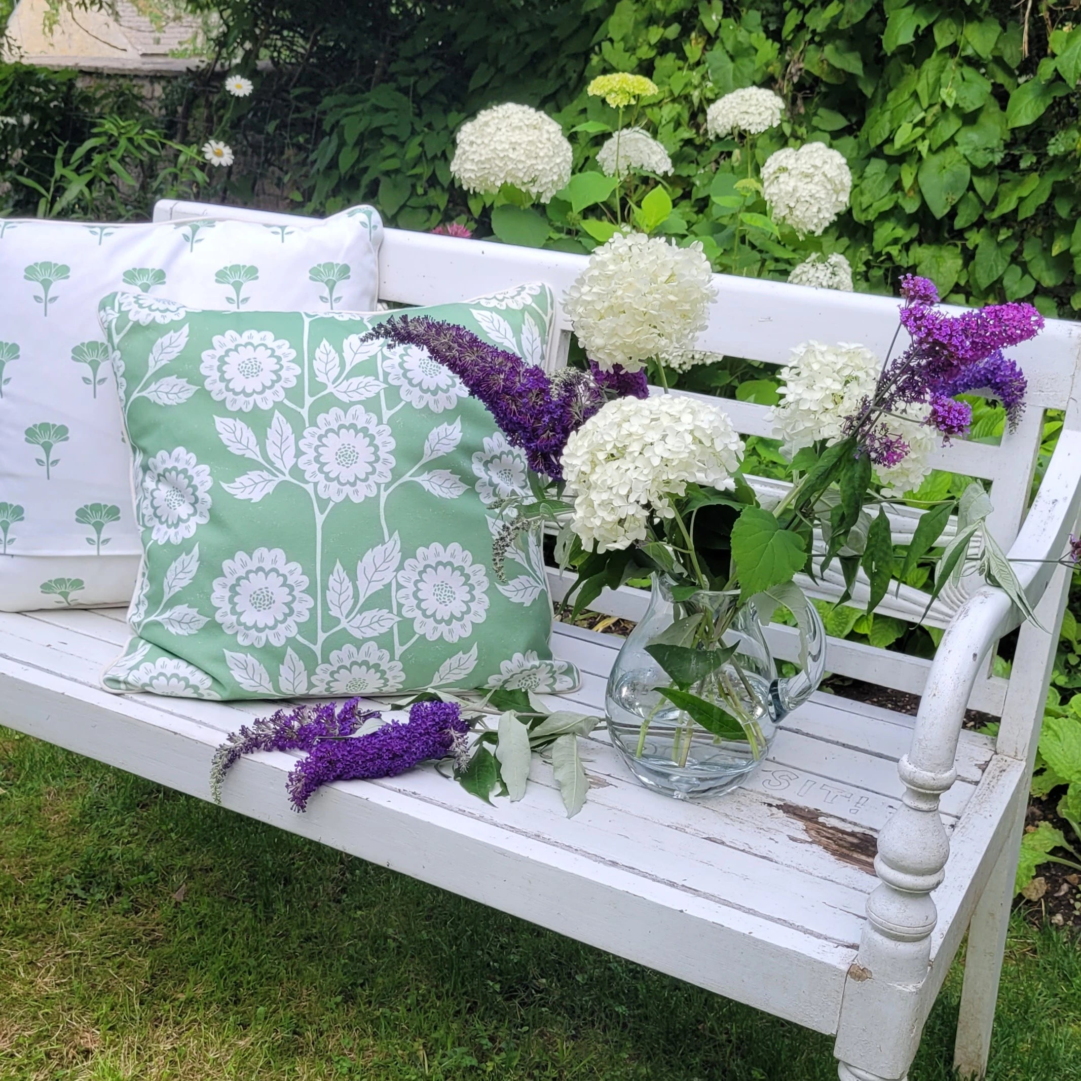 White bench with floral pillows and hydrangeas in a garden setting; cecilia design by lizzie mabley