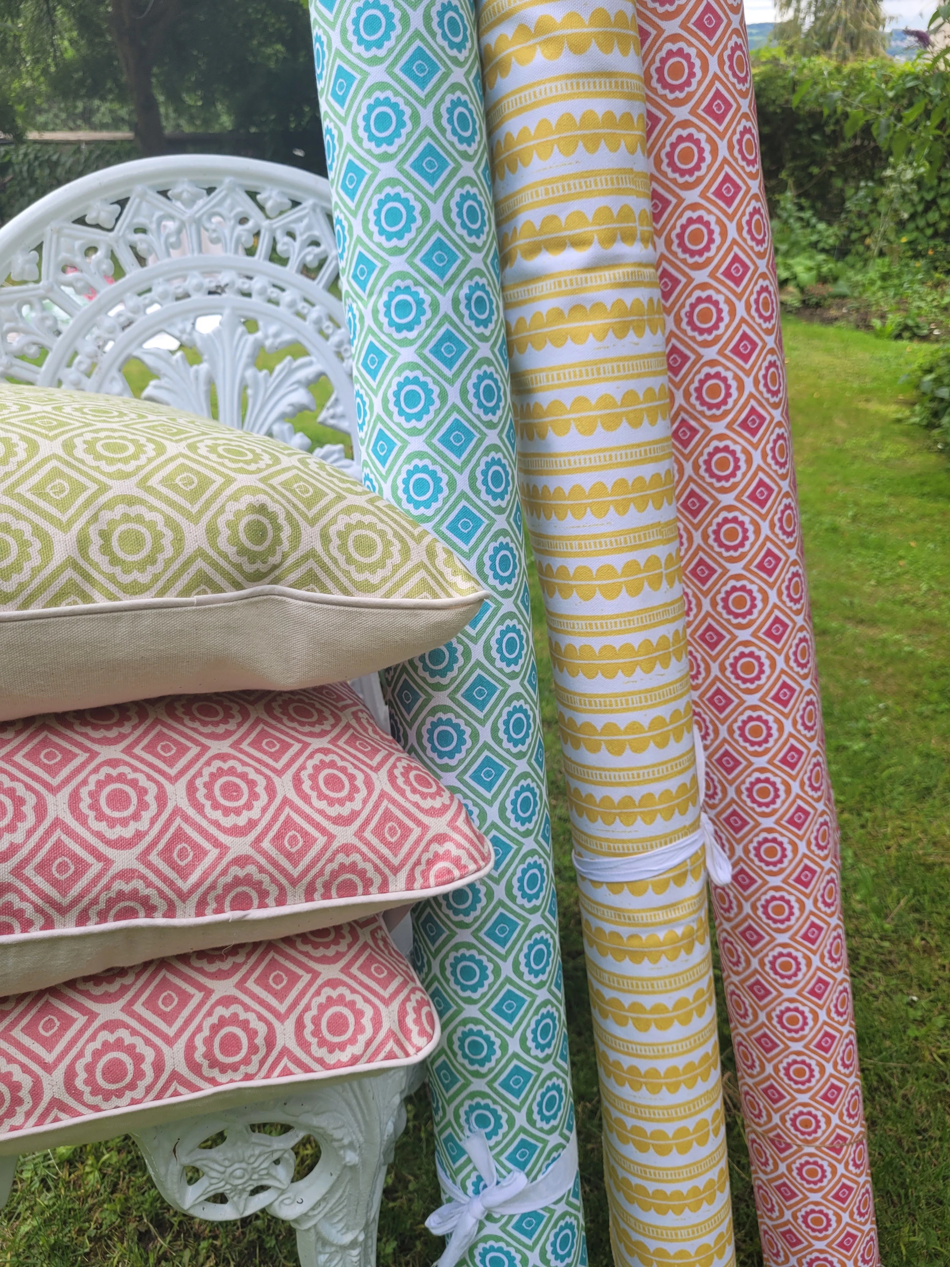 cushions and rolls of lino block printed fabric on a garden chair in rebecca, bright rebecca and henry designs by lizzie mabley