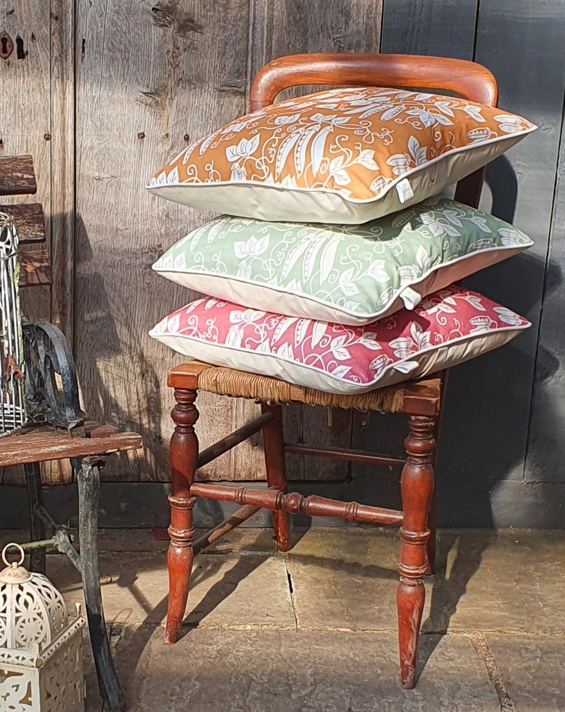 Stack of peas design cushions by Lizzie Mabley on a wooden chair against a rustic wooden wall.