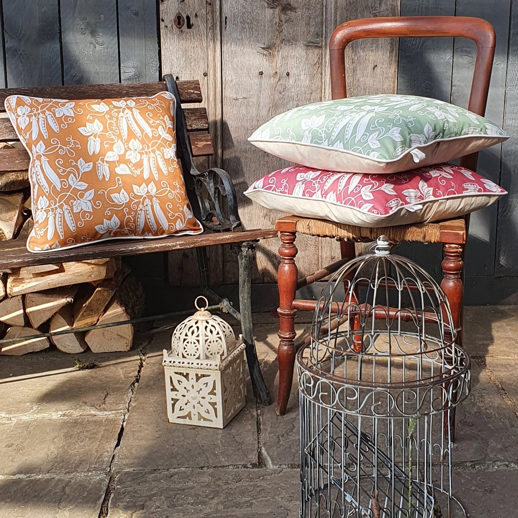 Stack of peas design cushions by Lizzie Mabley on a wooden chair against a rustic wooden wall.