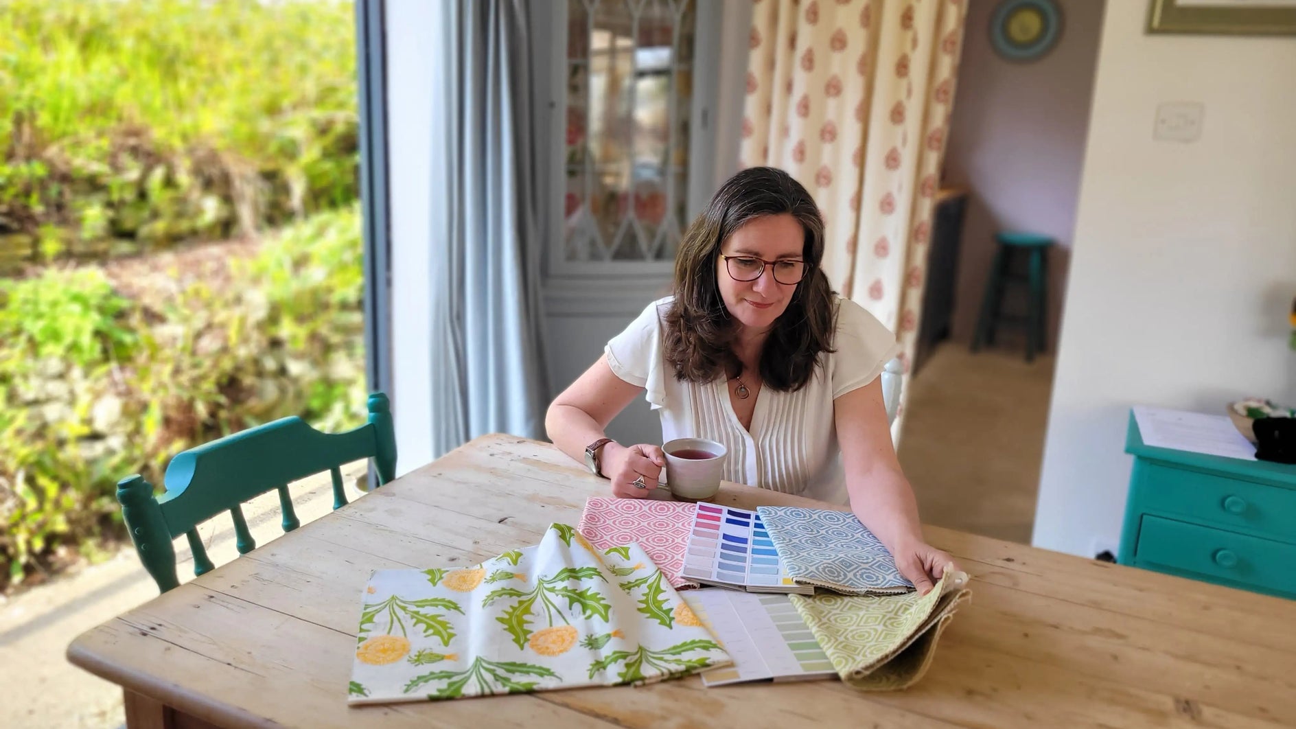 lizzie mabley sitting at antique dining table inspecting printed rebecca and dandelion designs