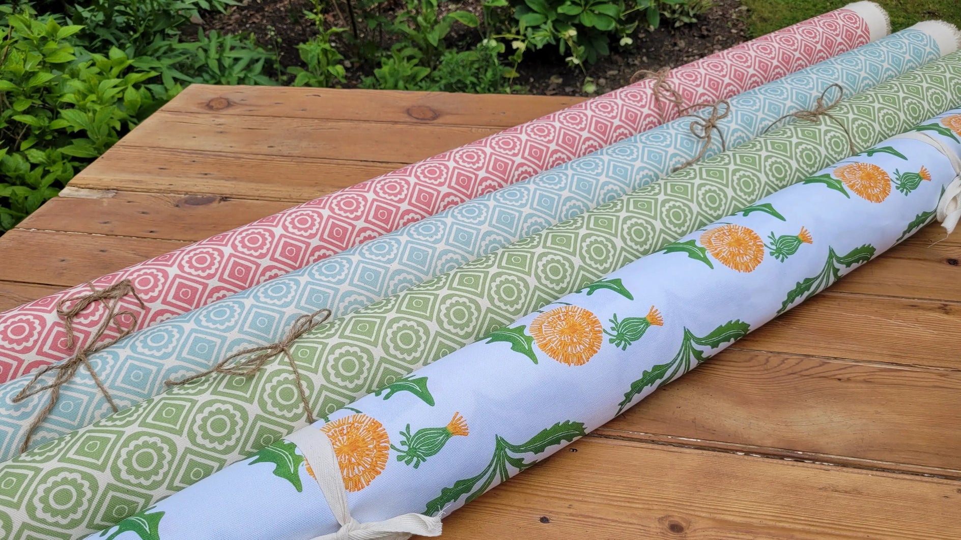rebecca and dandelion fabric rolls  designed by lizzie mabley laid on a rustic outdoor wooden table