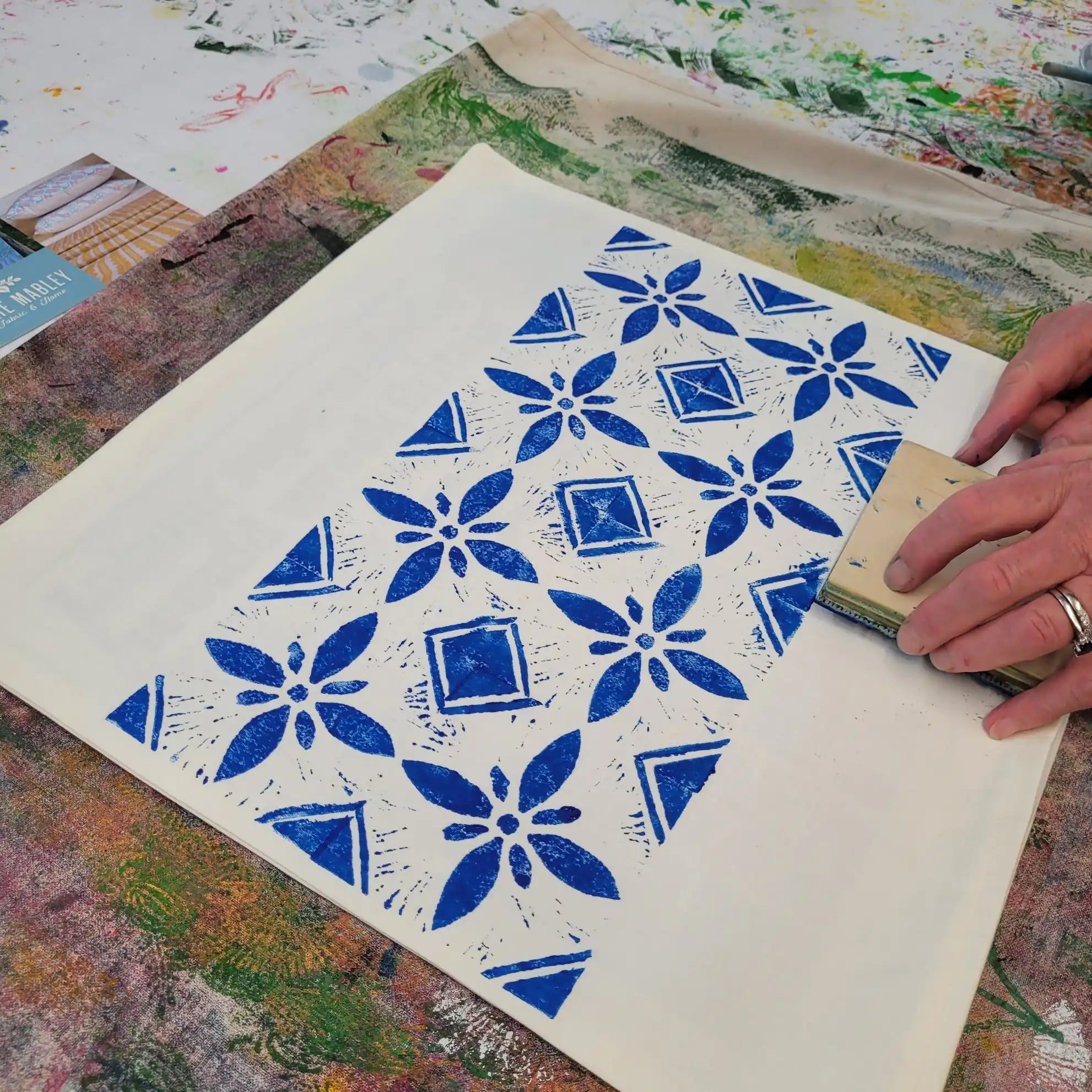 Hand printing a blue floral pattern onto white paper with a wooden lino block.